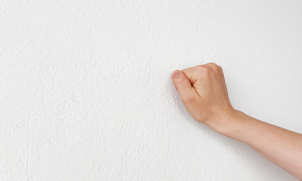 Hand die gegen eine verputze Wand klopft um den Untergrund dahinter zu bestimmen. Der sogenannte Klopftest